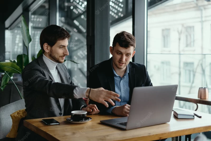 Two businessmen pointing laptop screen while discussing Free Photo