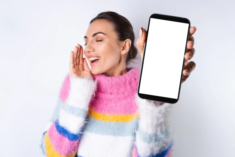 Young cheerful girl in a bright colored sweater on a white background holds a big phone in focus