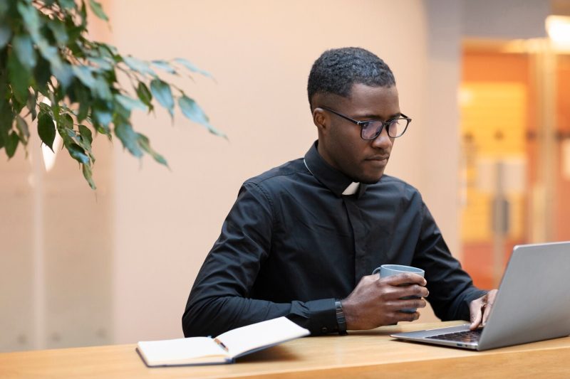 Young male priest using laptop at a cafe Free Photo