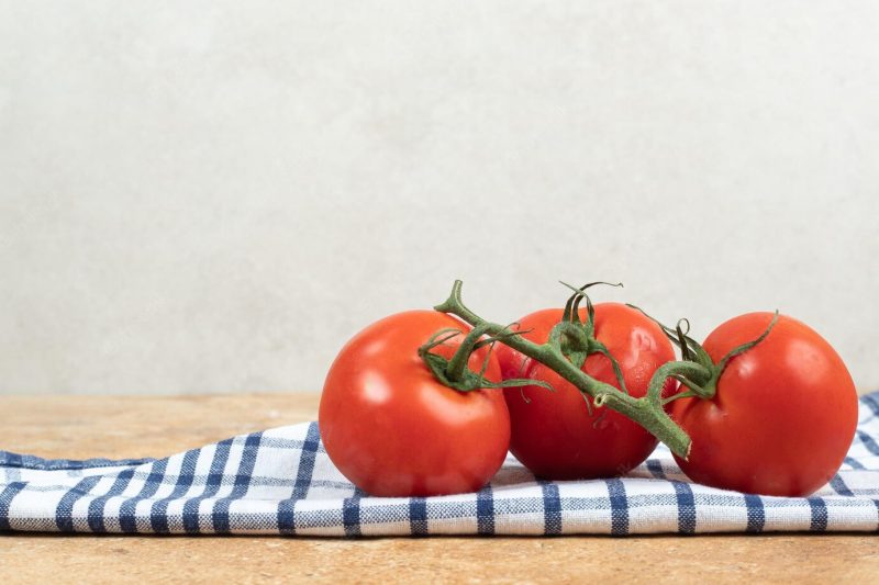 Bunch of fresh, red tomatoes with green stems on tablecloth Free Photo