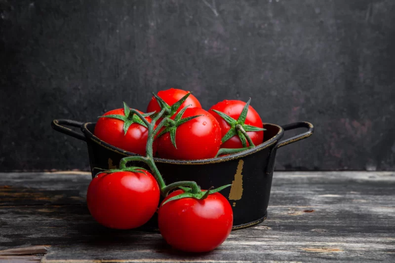 A bunch of tomatoes in a pot on a old wooden and black background. side view. Free Photo