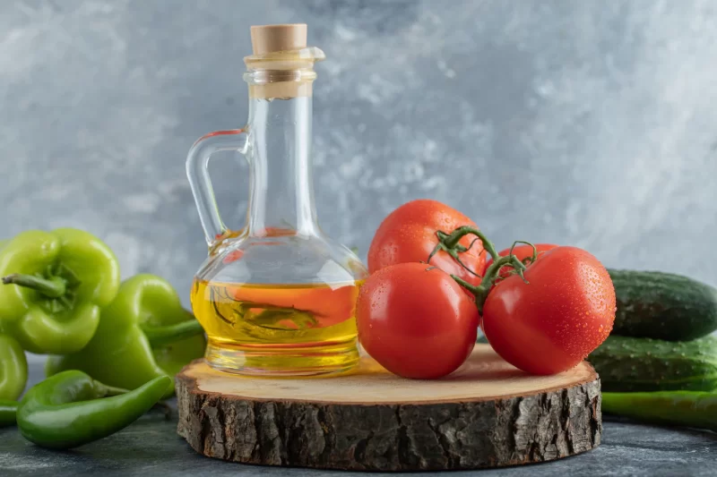 Close up photo of red tomato with green peppers and bottle of oil Free Photo