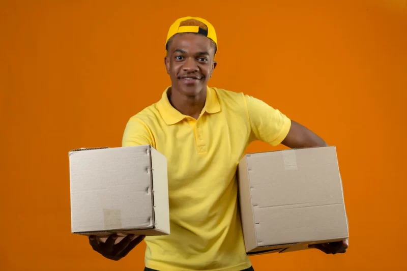 Delivery african american man in yellow polo shirt and cap standing with cardboard box