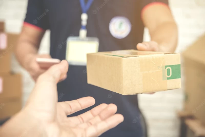 Delivery man smiling and holding a cardboard box Free Photo