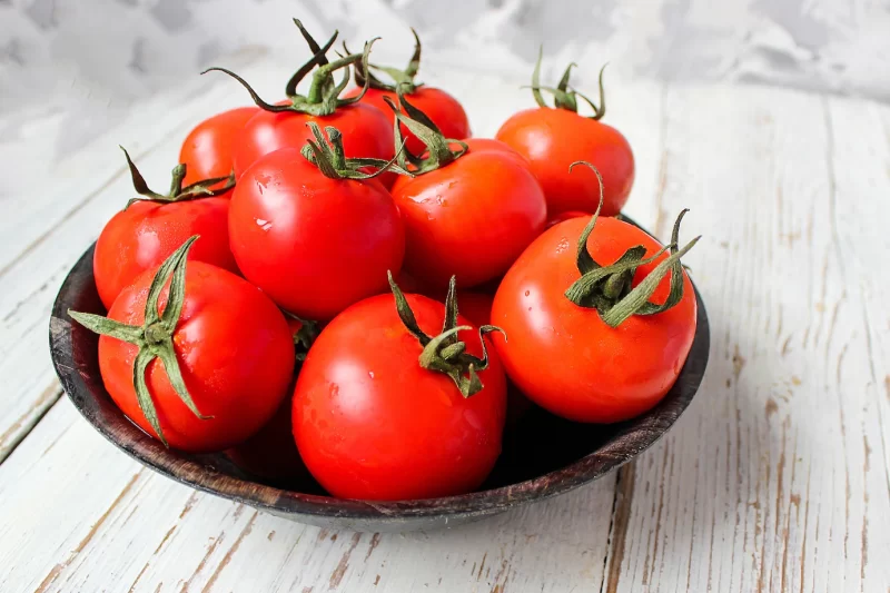 Fresh organic red tomatoes in black plate on white wooden table with green and red and chili peppers, green peppers, black peppercorns, salt, close up, healthy concept Free Photo