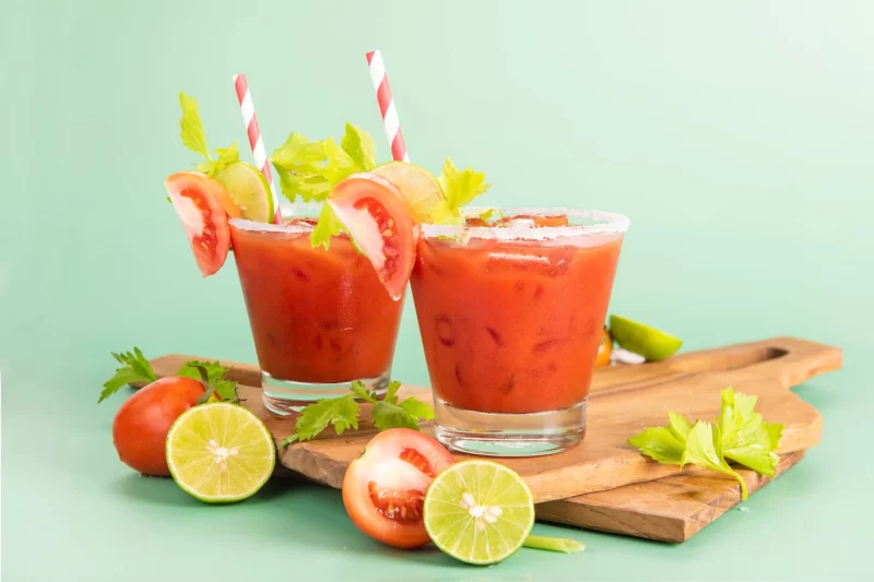 Glass glass of tomato juice, lime with fresh bright bunch of tomatoes isolated on green background, green parsley. vegetable drink. Free Photo