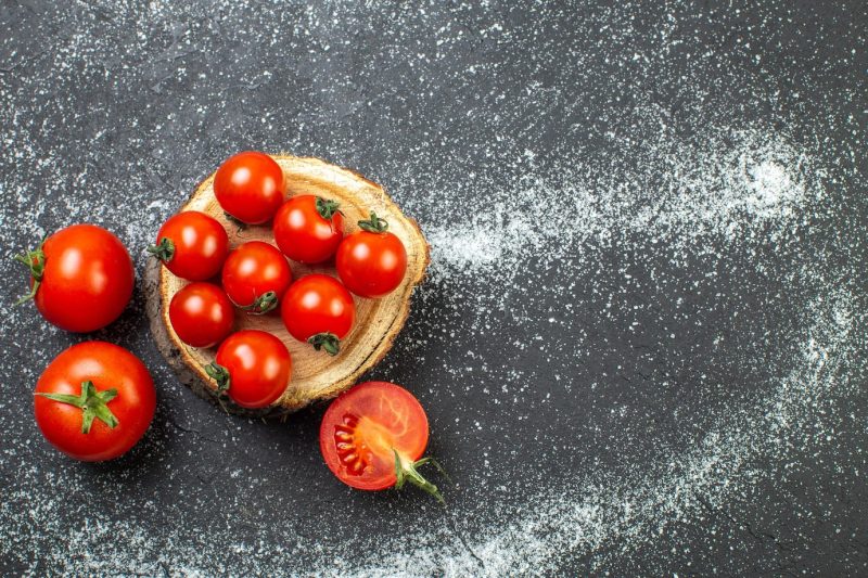 Overhead view of fresh tomatoes with stems on wooden board on the right side on white black background Free Photo