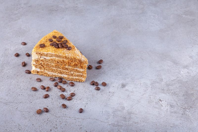 Slice of layered honey cake with coffee beans placed on a stone background . Free Photo