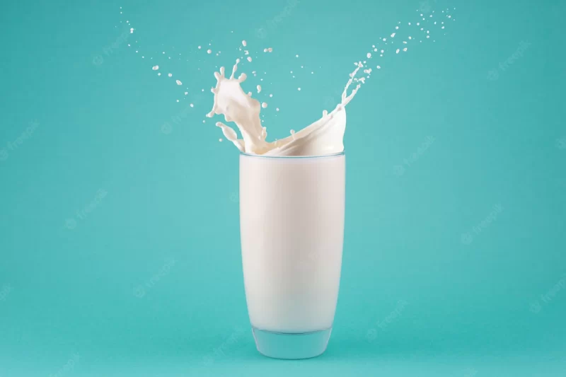 Splashes of milk in a glass isolated on blue background Premium Photo