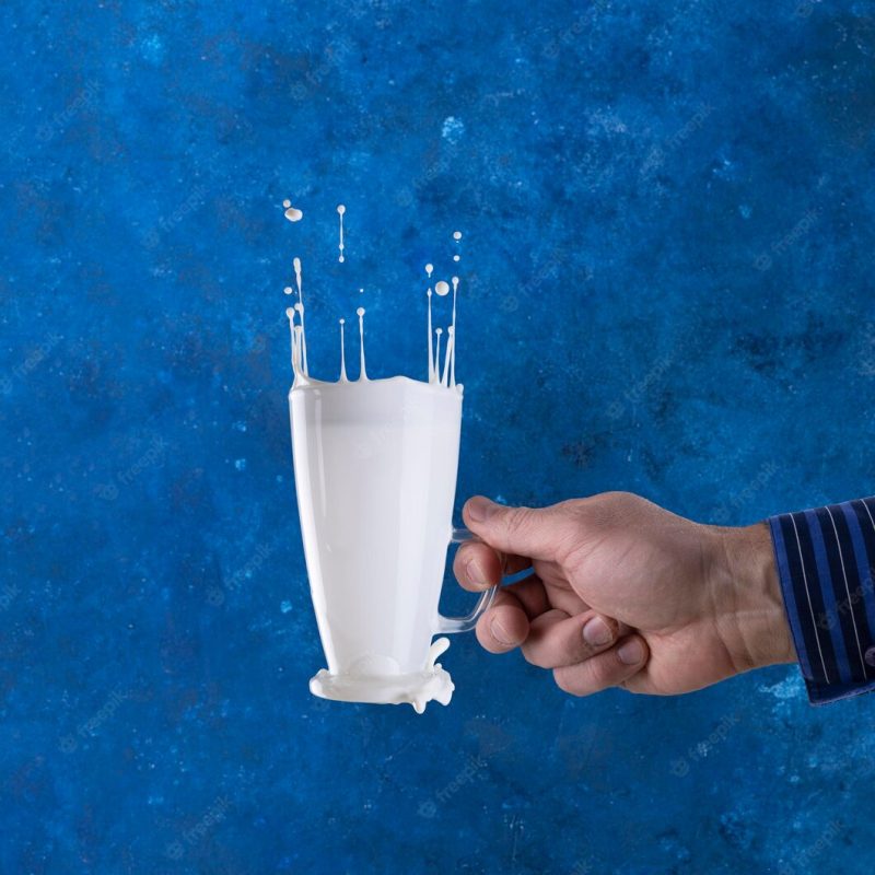 Splashes of milk in a glass levitation on a blue background with a hand Premium Photo