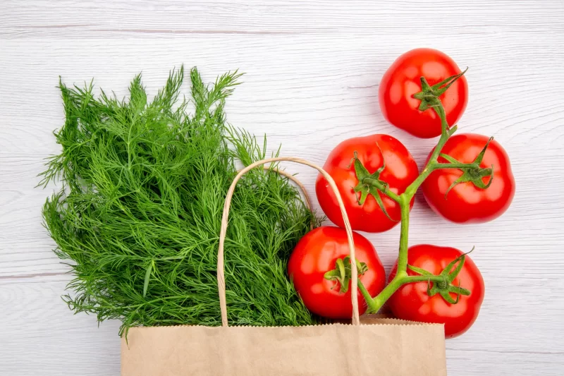 Top view of a bundle of green onion in a basket and tomatoes with stem on white background Free Photo