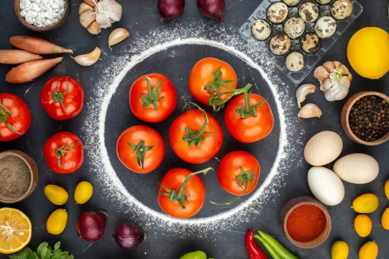 Top view of dinner preparation with fresh vegetables eggs flour lemon kumquats spices on black background Free Photo