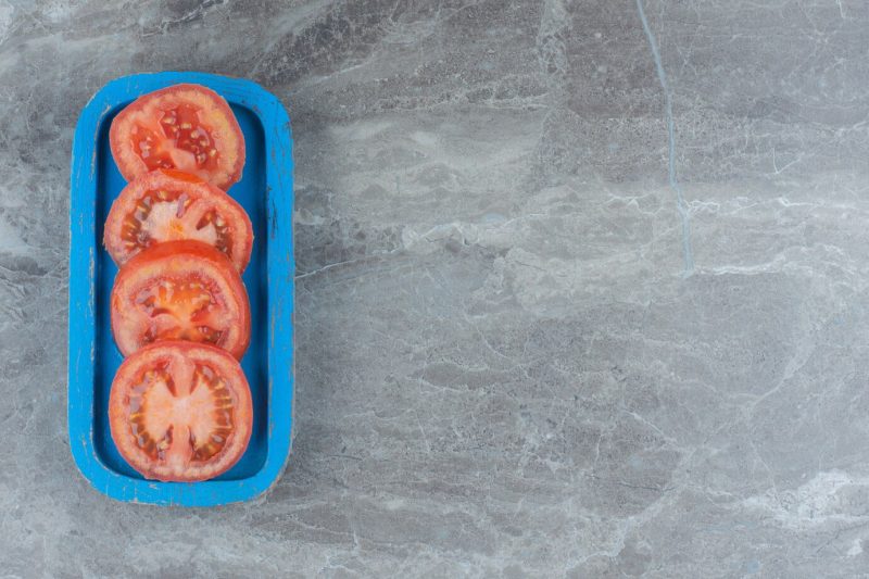 Top view of fresh organic tomato slices on blue wooden board Free Photo