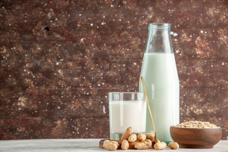 Top view of glass bottle and cup filled with milk on wooden tray and dry fruits spoon oats in brown