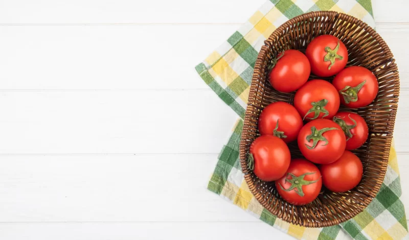 Top view of tomatoes in basket on cloth on right side and white surface with copy space Free Photo