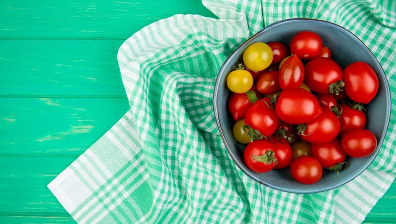 Top view of tomatoes in bowl on cloth on right side and green surface Free Photo