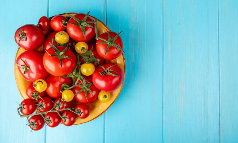 Top view of tomatoes in bowl on left side and blue surface with copy space Free Photo