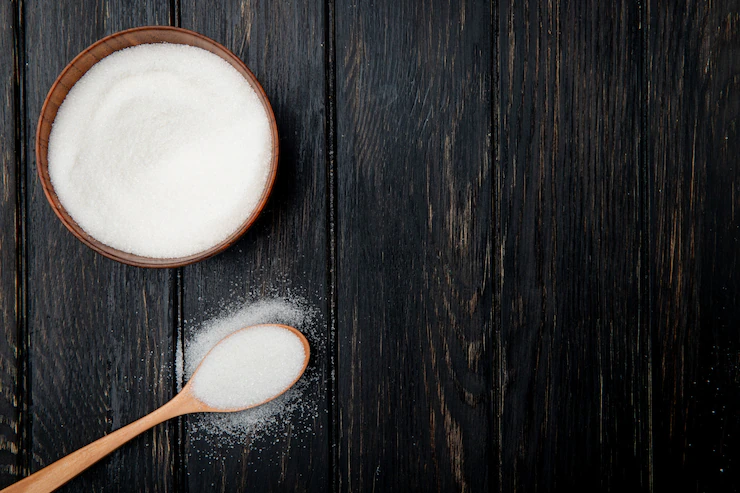 Top view of white granulated sugar in a wooden bowl and in a wooden spoon on black rustic background with copy space Free Photo