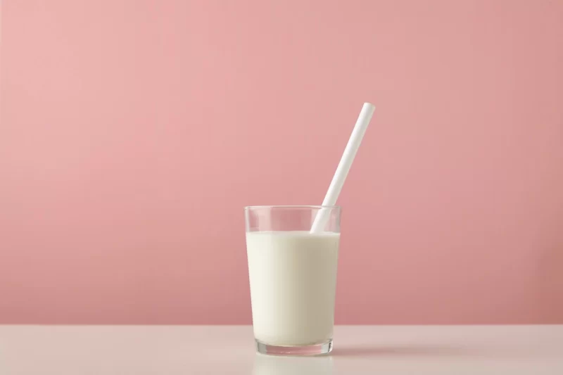 Transparent glass with fresh organic milk and white drinking straw inside isolated on pastel pink background on wooden table Free Photo