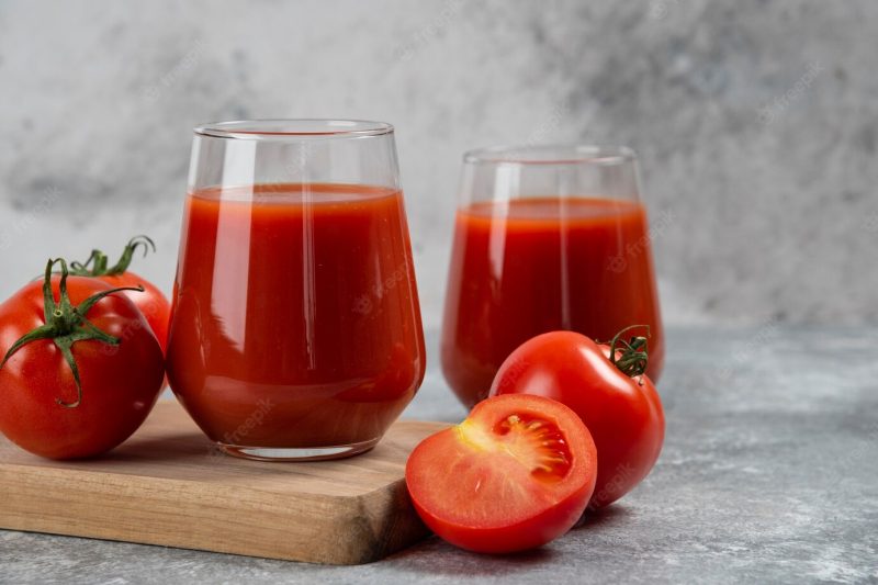 Two glass cups of tomato juice on a wooden board. Free Photo