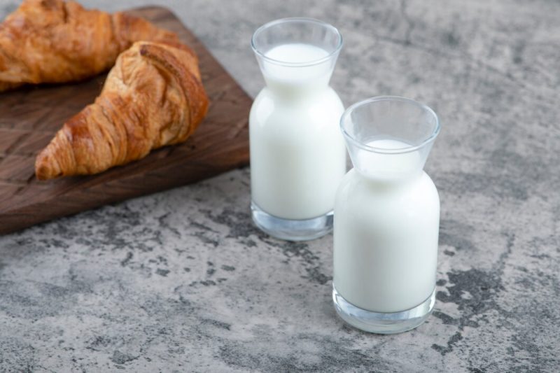 A wooden cutting board of fresh croissants and white glass pitchers of milk . Free Photo