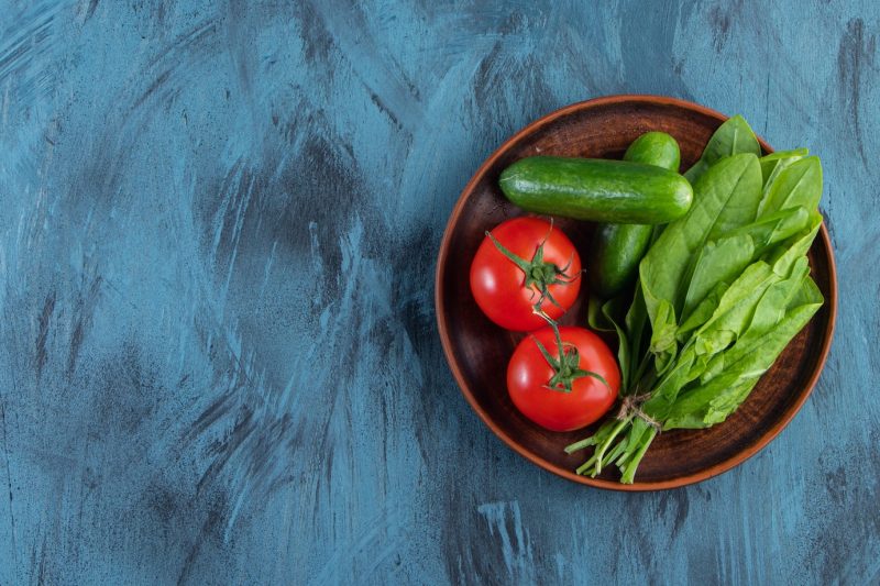 Wooden plate of fresh tomatoes, cucumbers and greens on blue background. Free Photo