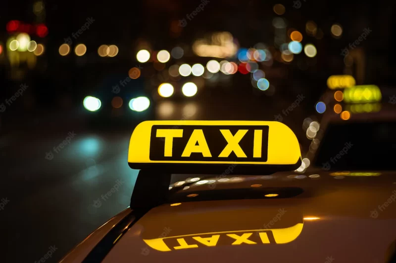 Yellow and black sign of taxi placed on top of a car at night Free Photo