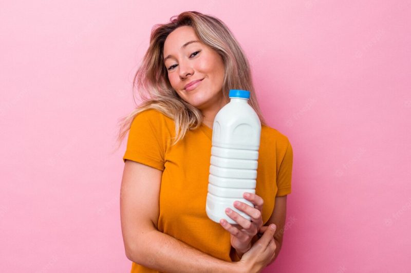 Young australian woman holding a bottle of milk isolated on pink background laughing and having fun. Premium Photo