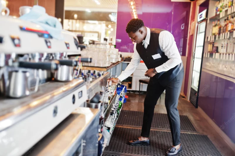 African American bartender at bar holding bottle of alcoholic beverage preparation Free Photo