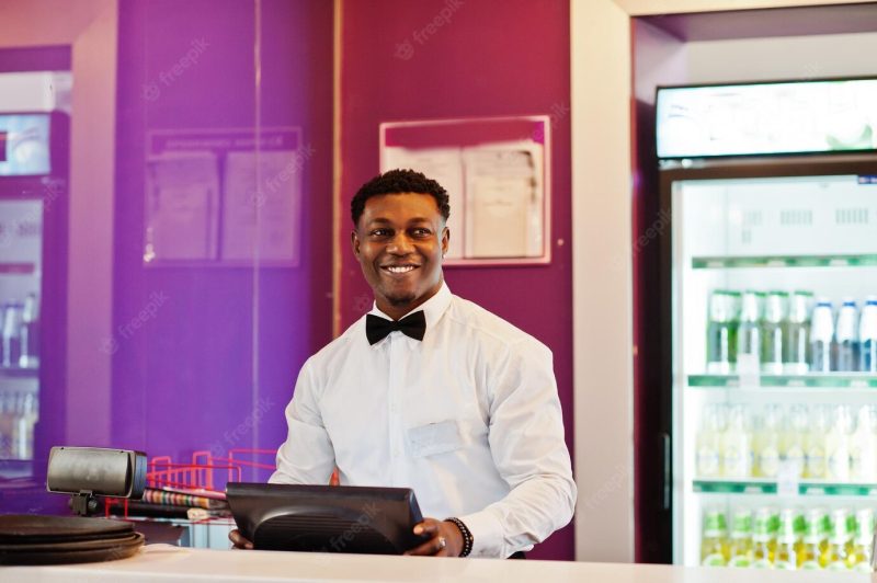 African American bartender wearing bow tie using cash terminal screen at bar Free Photo