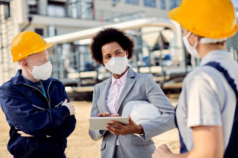 African american building contractor talking to civil engineers at construction site during coronavirus epidemic Free Photo