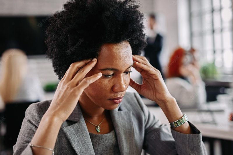 African American business woman having a headache and feeling displeased because of the problems she has at work there are people in the background Free Photo