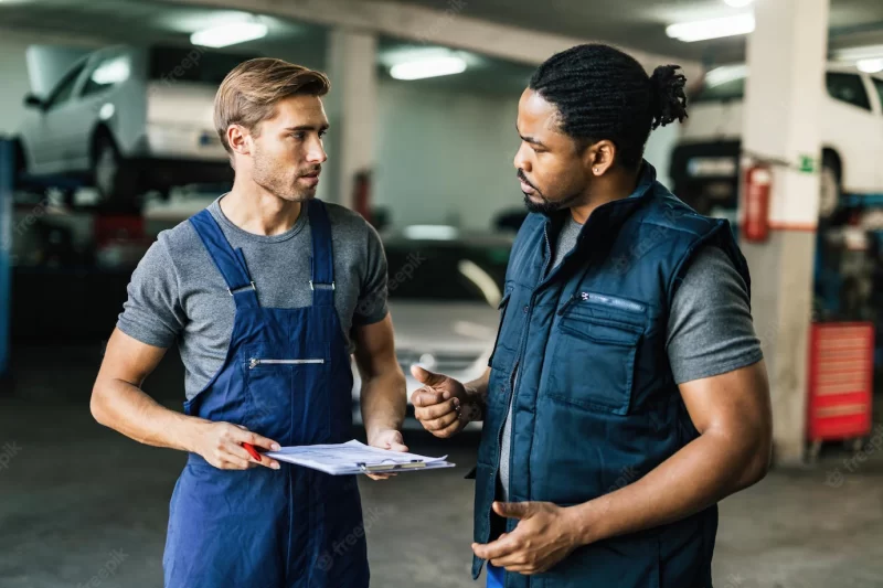 African american car mechanic and his coworker communicating in auto repair shop Free Photo