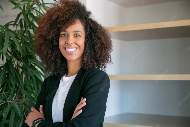 African american curly businesswoman standing with folded hands. portrait of successful confident young pretty female office employer in suit posing at work. business, company and management concept Free Photo