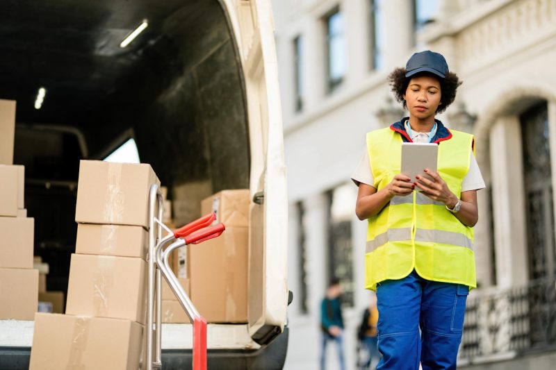 African American deliverer using digital tablet while unloading packages from a van Free Photo