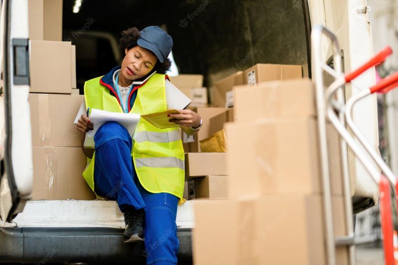 African american delivery woman talking on the phone while going through delivery list in a van Free Photo