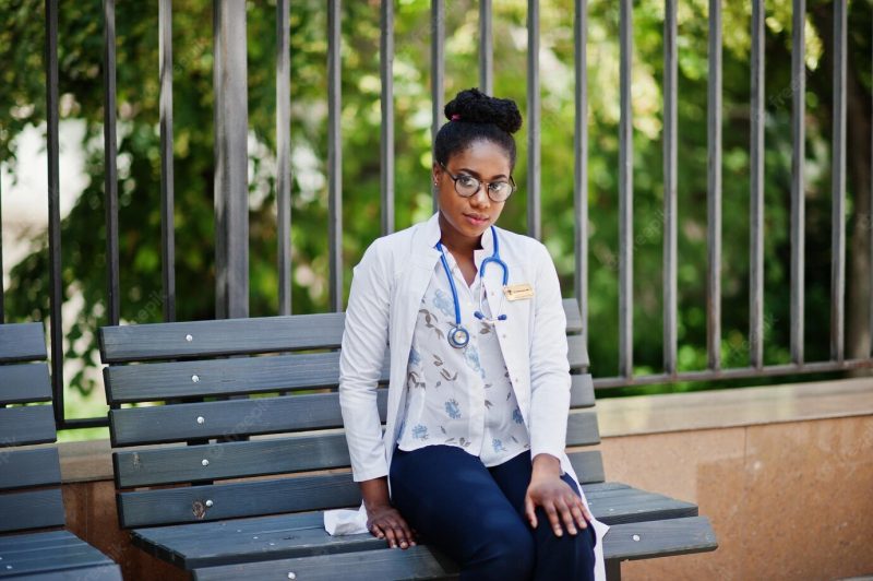 African american doctor female at lab coat with stethoscope posed outdoor sitting on bench Free Photo