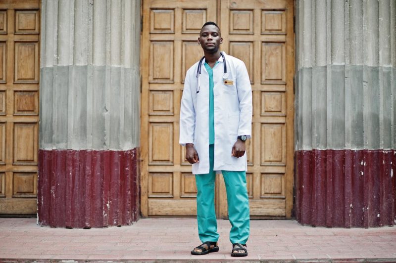 African american doctor male at lab coat with stethoscope outdoor against clinic door Free Photo