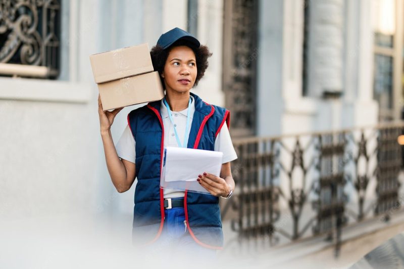 African american female courier standing on the street with packages and clipboard while making delivery in the city Free Photo