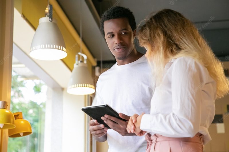 African American guy looking at blonde client and holding tablet Free Photo