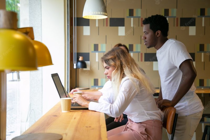 African American guy standing behind blonde woman and looking at screen Free Photo