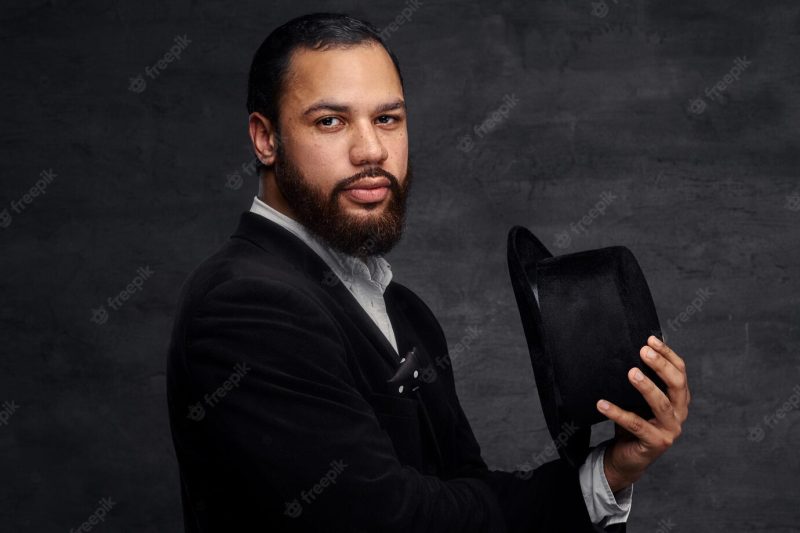 African-american man in an elegant suit, holds a black hat. isolated on a dark background. Free Photo