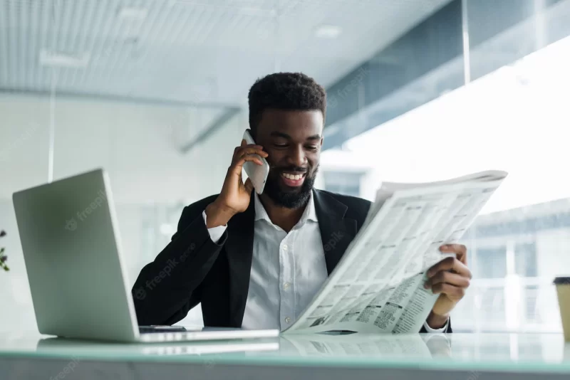 African american man reading newspaper and talking on phone in office Free Photo