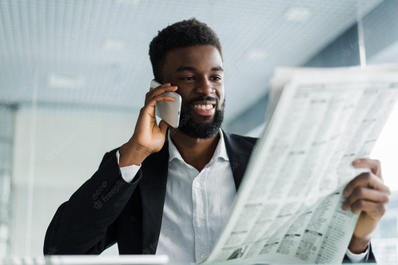 African american man reading newspaper and talking on phone in office Free Photo