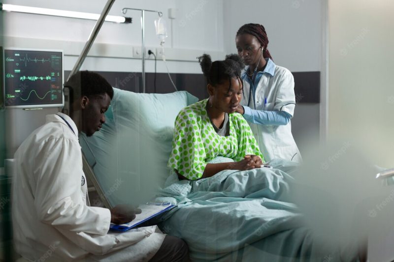 African american medical team working on healing patient in hospital ward bed. man and woman with doctors occupation examining young adult for treatment using monitor and stethoscope Free Photo