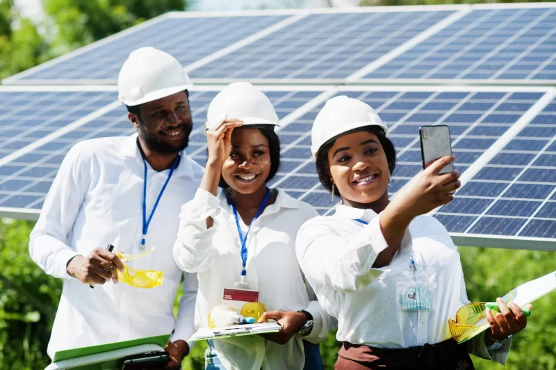 African american technician checks the maintenance of the solar panels group of three black engineers meeting at solar station make selfie by phone Free Photo