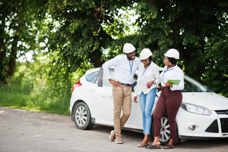 African american technician in white helmets near car group of three black engineers meeting Free Photo