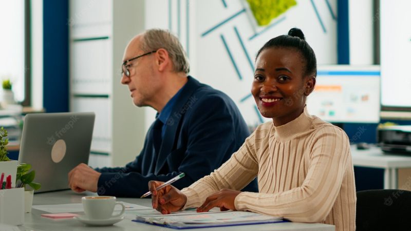 African businesswoman analysing report and looking at camera smiling sitting at conference desk during brainstorming. entrepreneur working in professional start up financial business ready for meeting Free Photo