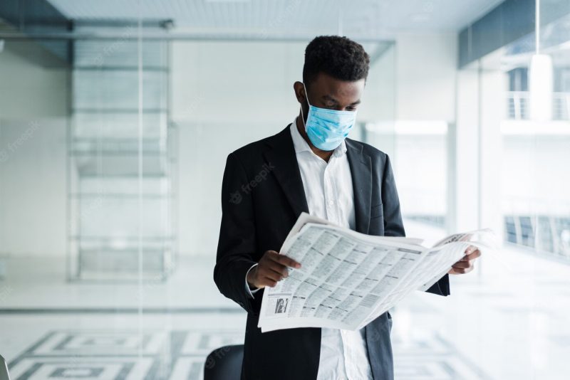 African handsome business man in medical mask reading the newspaper at office building Free Photo