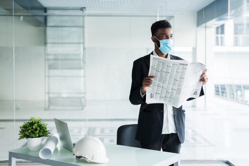 African handsome business man in medical mask reading the newspaper at office building Free Photo